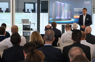 A speaker delivers a professional presentation to an audience in a modern conference room, with a technology-focused slide displayed on a screen.
