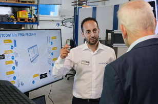 An expert demonstrates laser and 3D metrology technology to a visitor in an industrial environment.